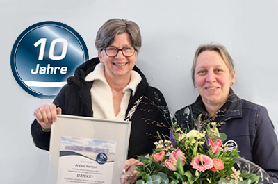 Andrea Kemper (links im Bild) und Teamleiterin Julia Böhnke (rechts im Bild) mit Urkunde und Blumenstrauß